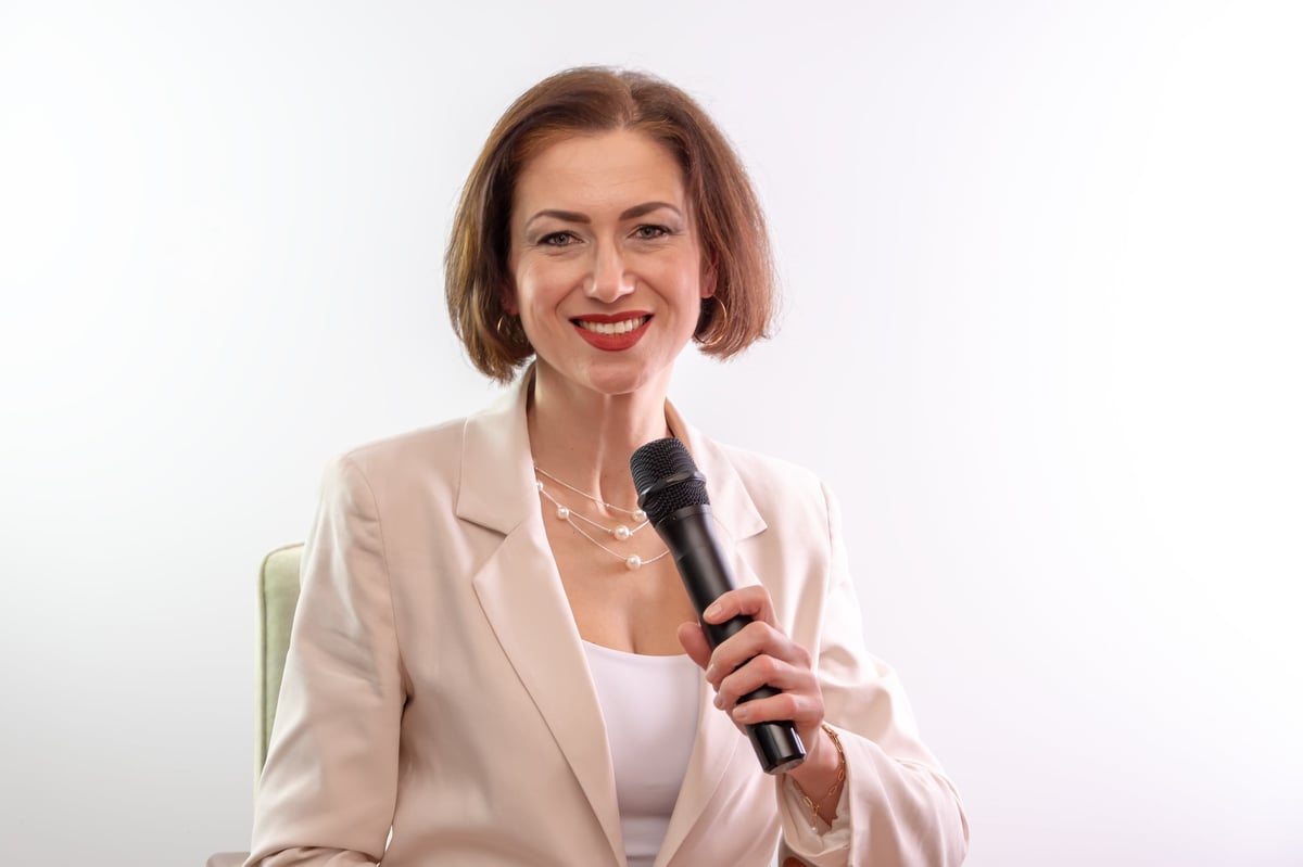 An emotional woman with a microphone is sitting in an armchair, showing a confident, friendly expression on her face