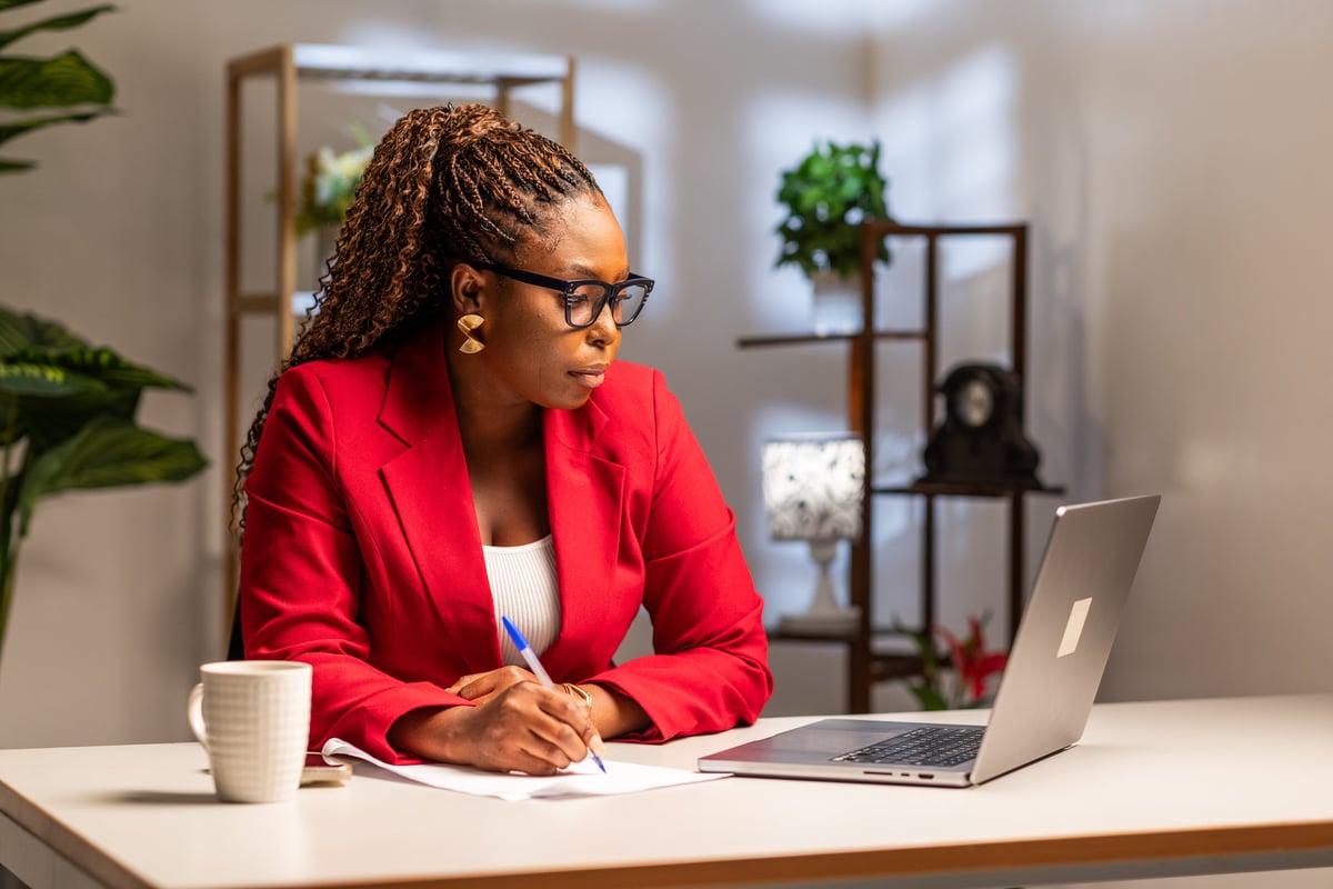 African corporate businesswoman writing notes while working at her home office on a laptop