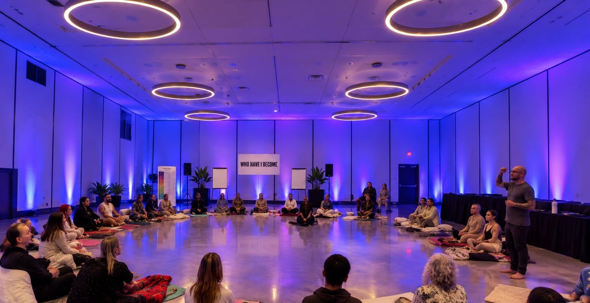 Modern event space with purple ambient lighting, circular seating arrangement, and potted plants creating an upscale gathering atmosphere