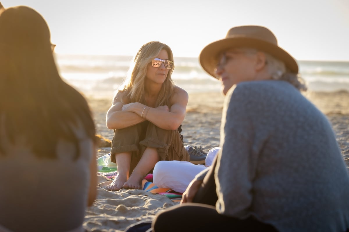 Group of people sitting together on a sandy beach during golden hour sunset