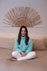Lisa Chastain seated cross-legged on a beige sofa in a turquoise turtleneck