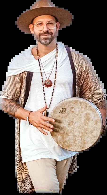 Man with beard wearing cowboy hat and glasses holding a frame drum with beaded necklaces and patterned cardigan