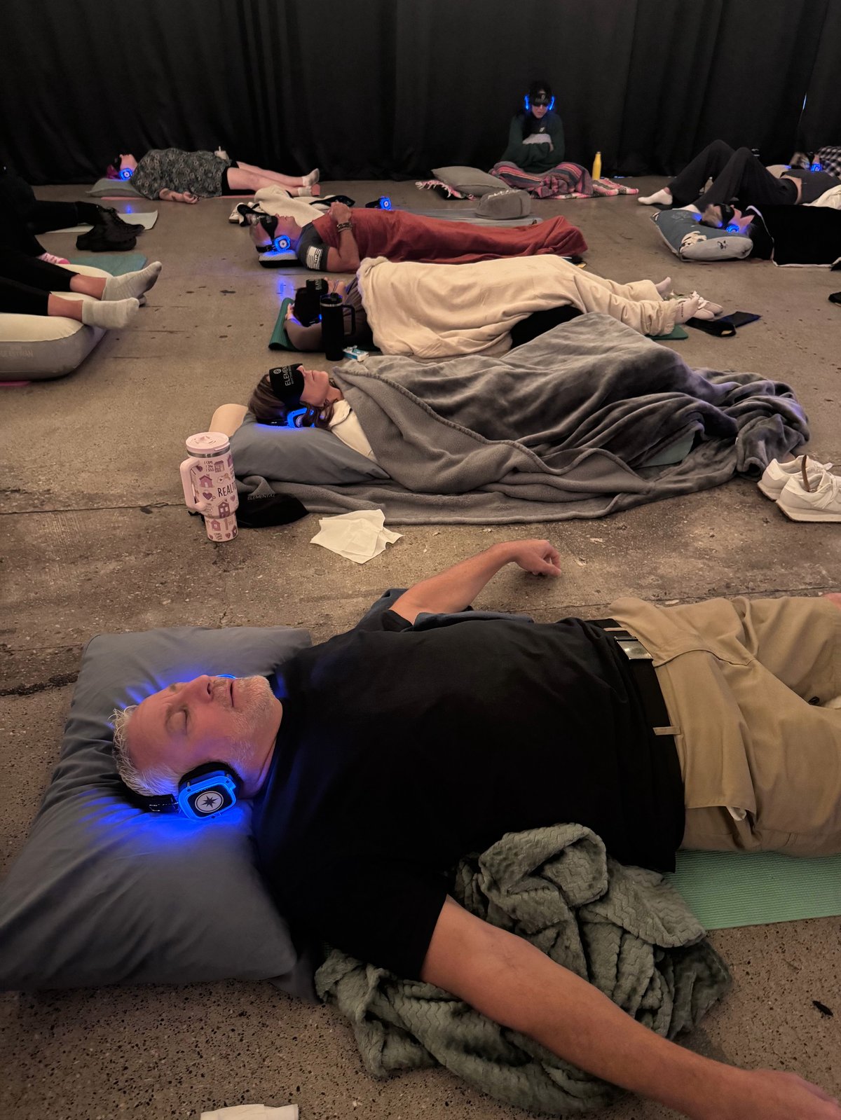 Group of people lying on floor during guided relaxation or meditation session in dark studio space