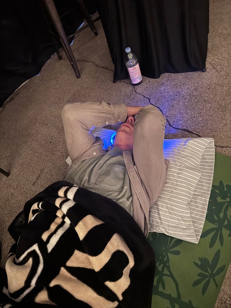 Person lying on carpet using a blue light therapy device on their knee while wearing khaki pants and black and white socks