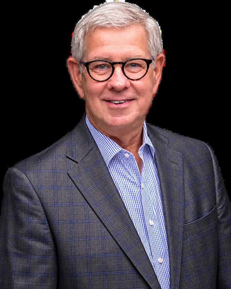 Older man wearing glasses and a plaid blazer over a blue striped shirt, smiling at the camera against a black background