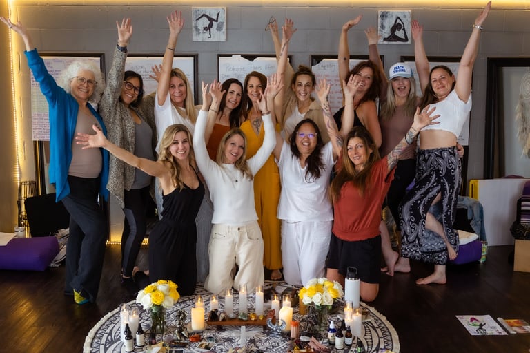 Group of diverse women celebrating together indoors with arms raised, yellow flowers and candles on a table in front