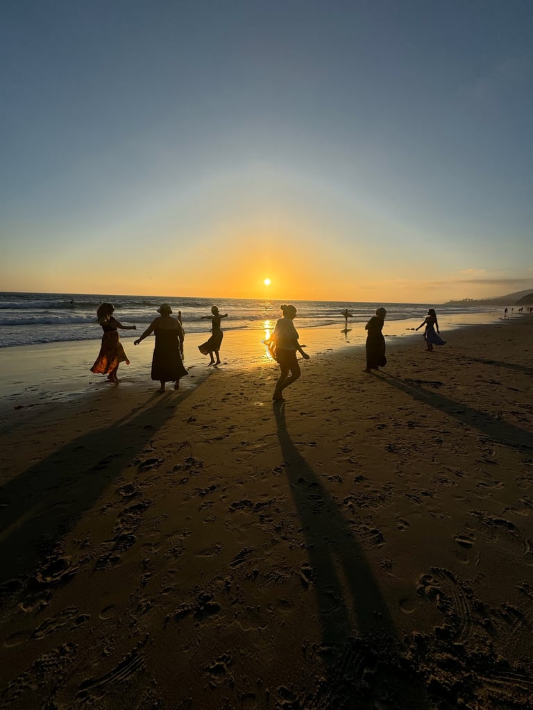 Silhouetted figures walking on sandy beach at sunset with golden sunlight reflecting on wet sand and ocean