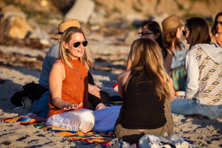 Group of young women sitting on beach sand, socializing together on a sunny day