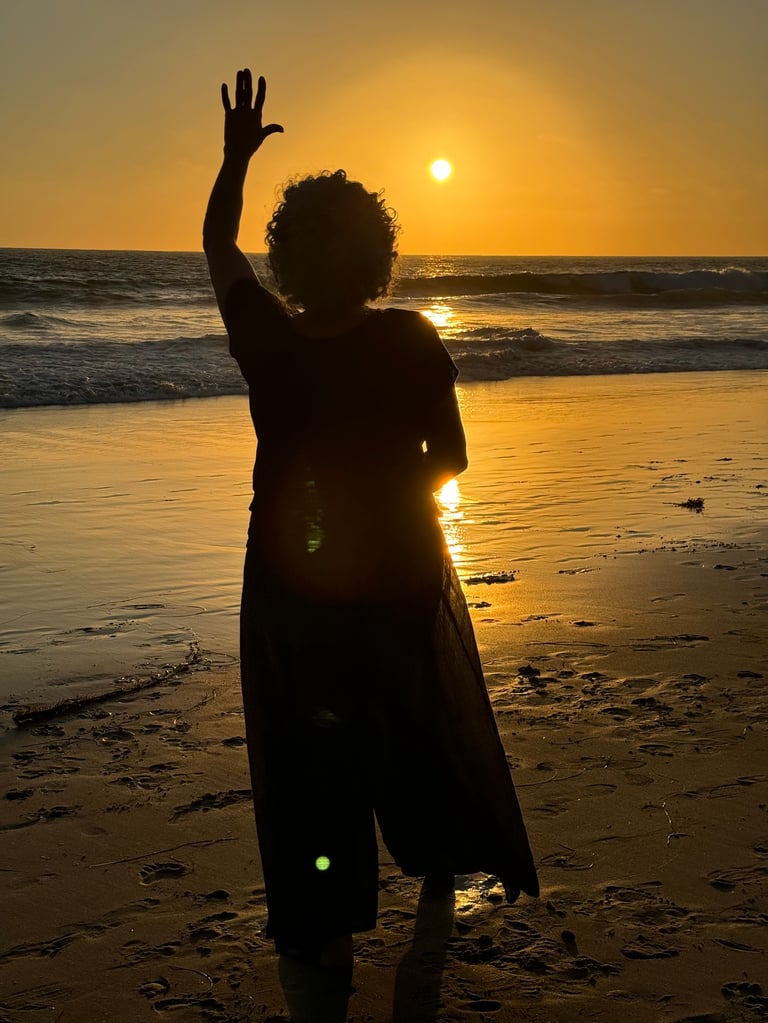 Silhouette of a person with raised arm standing on beach at sunset overlooking the ocean