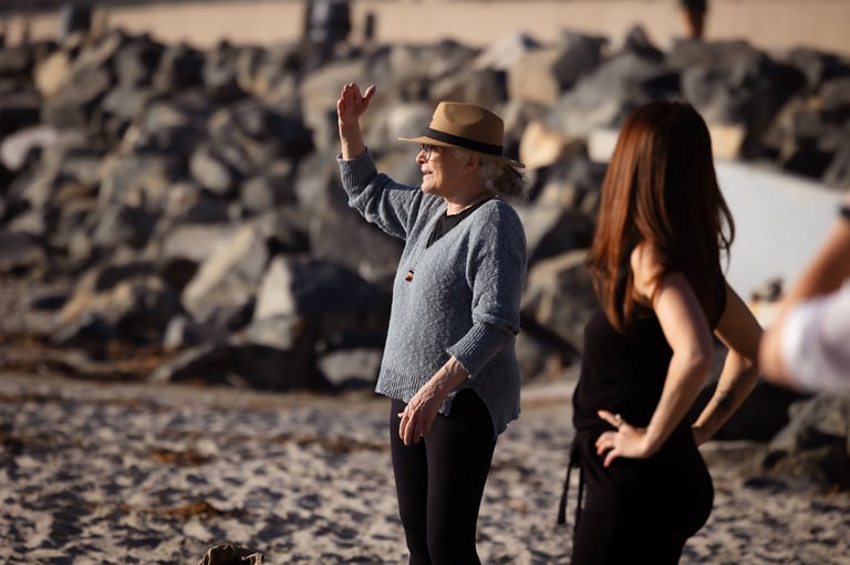 Man wearing cowboy hat and denim shirt waving on rocky beach with woman in black top beside him
