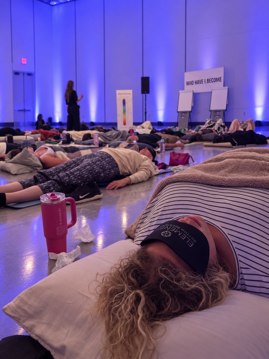 Group of people lying on floor in dimly lit room with blue lighting during a meditation or wellness event