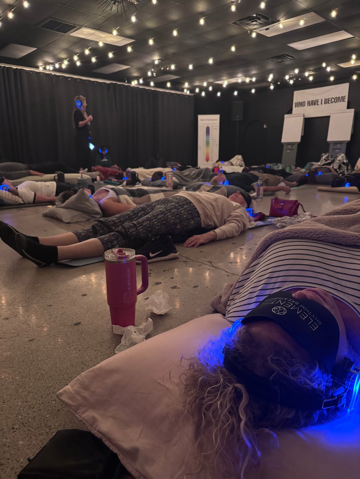 Group of people lying on floor during sound bath meditation session with blue ambient lighting and hanging lights overhead
