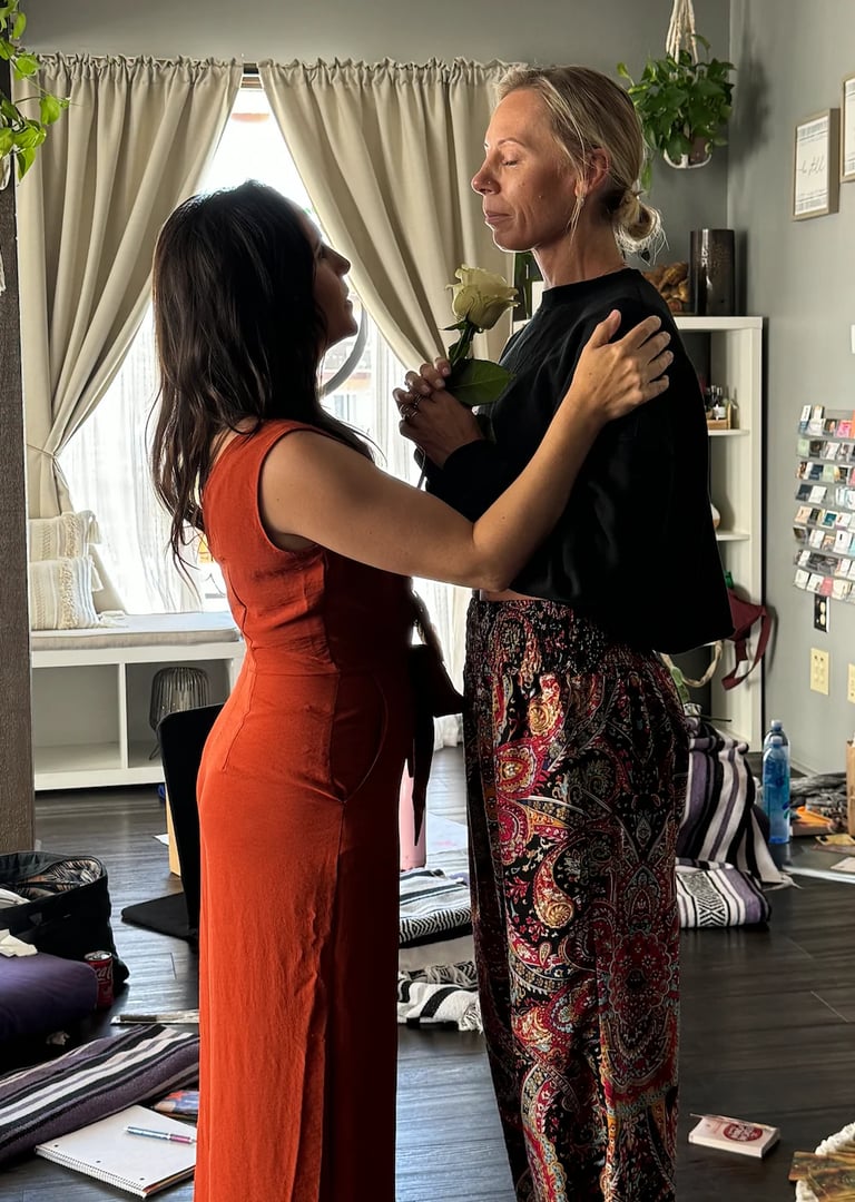 Two women dancing together in a bright studio space with plants and windows behind them