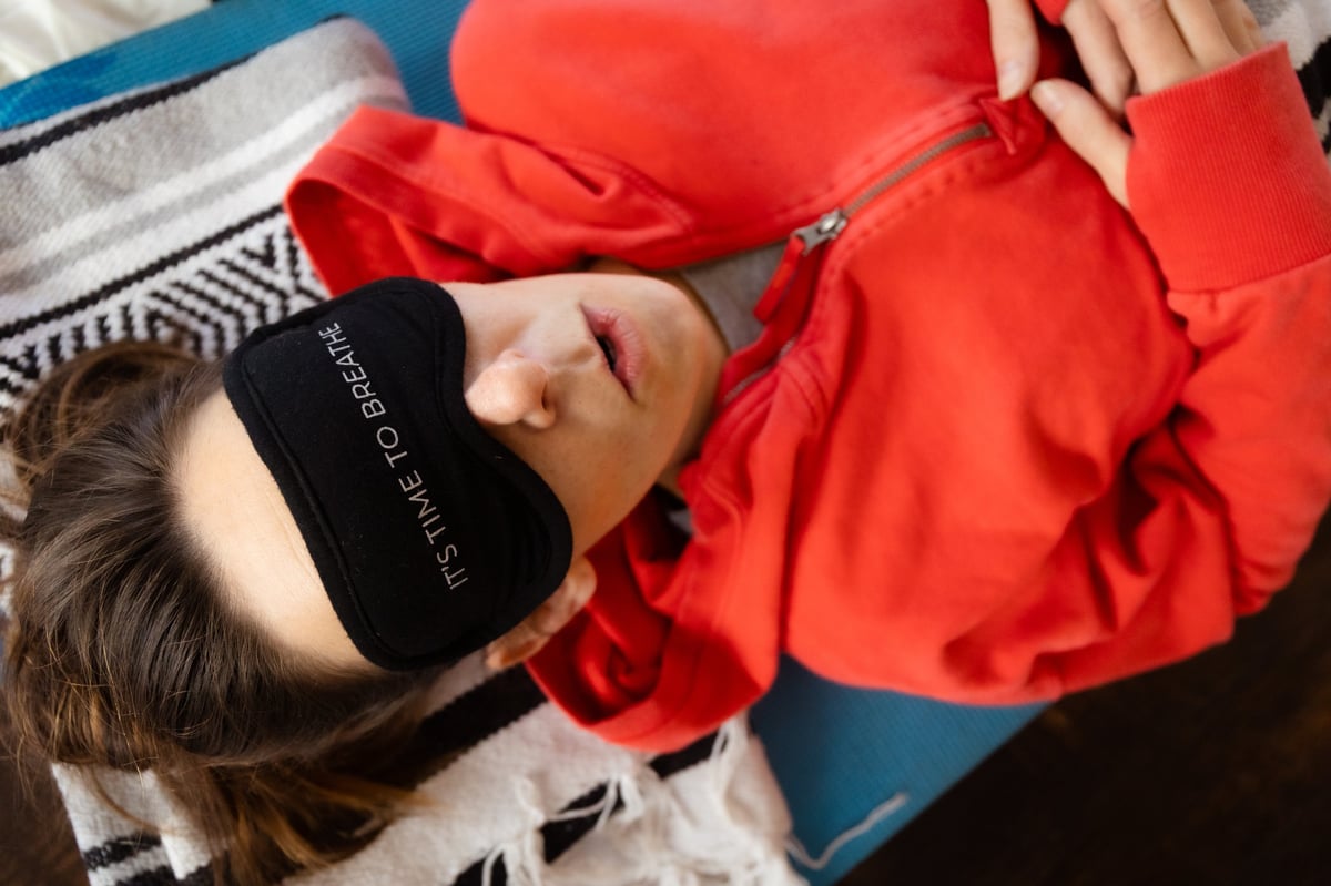 Person lying down wearing a red jacket and black sleep mask