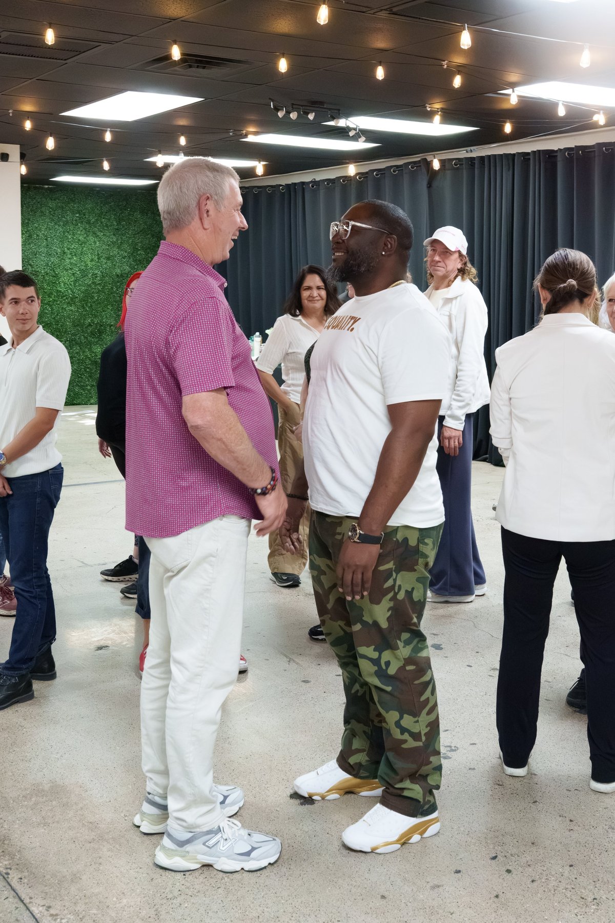 Two men conversing in a modern indoor venue with other people mingling in the background