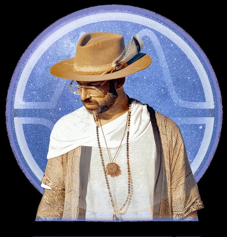 Man wearing tan cowboy hat, white shirt, and tan patterned vest with beaded necklace against blue circular background